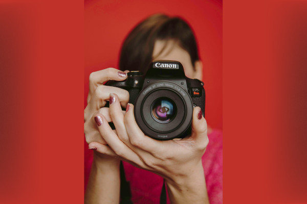 Close-up of a person holding a Canon camera against a red background, lens centered and in focus.